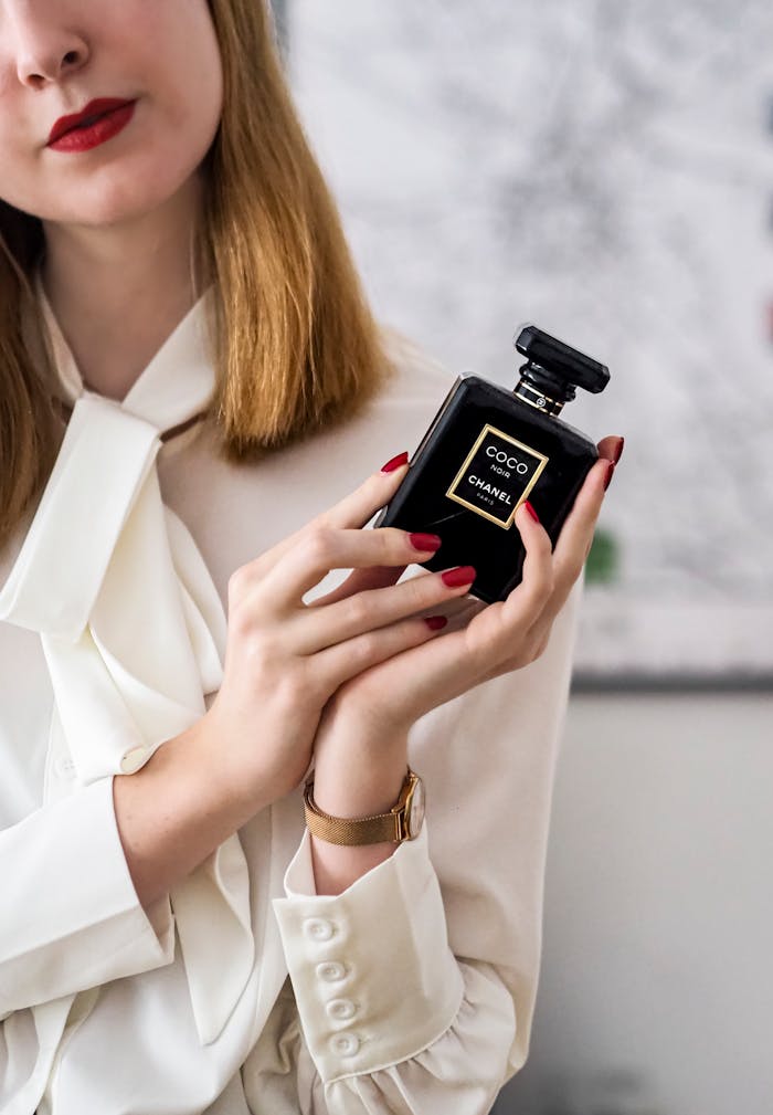 Stylish woman in white blouse holding a luxury perfume bottle with red nails.
